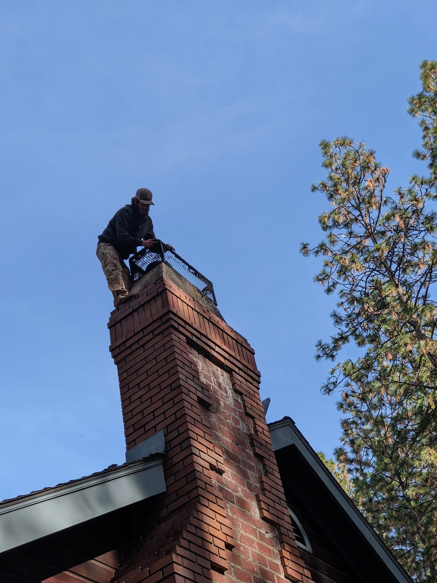 Technician installing a chimney cap on a brick chimney